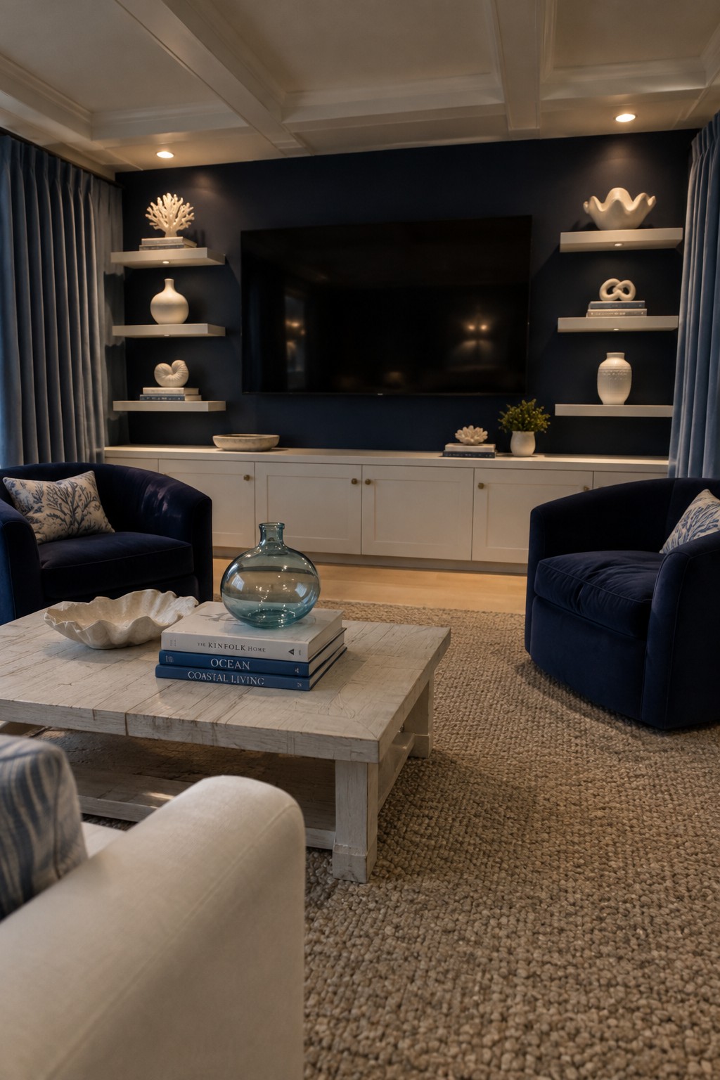 A living room with navy built-in shelving, white lower cabinets, two blue armchairs, and a pale wood coffee table.