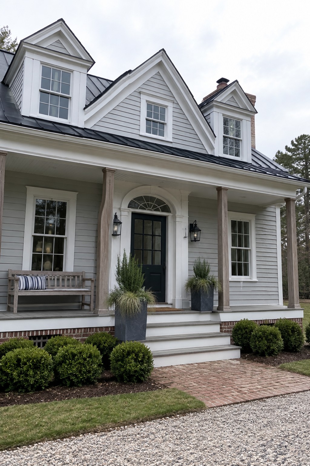 A light gray clapboard house with white trim, three front dormers, a covered porch, and a black front door.