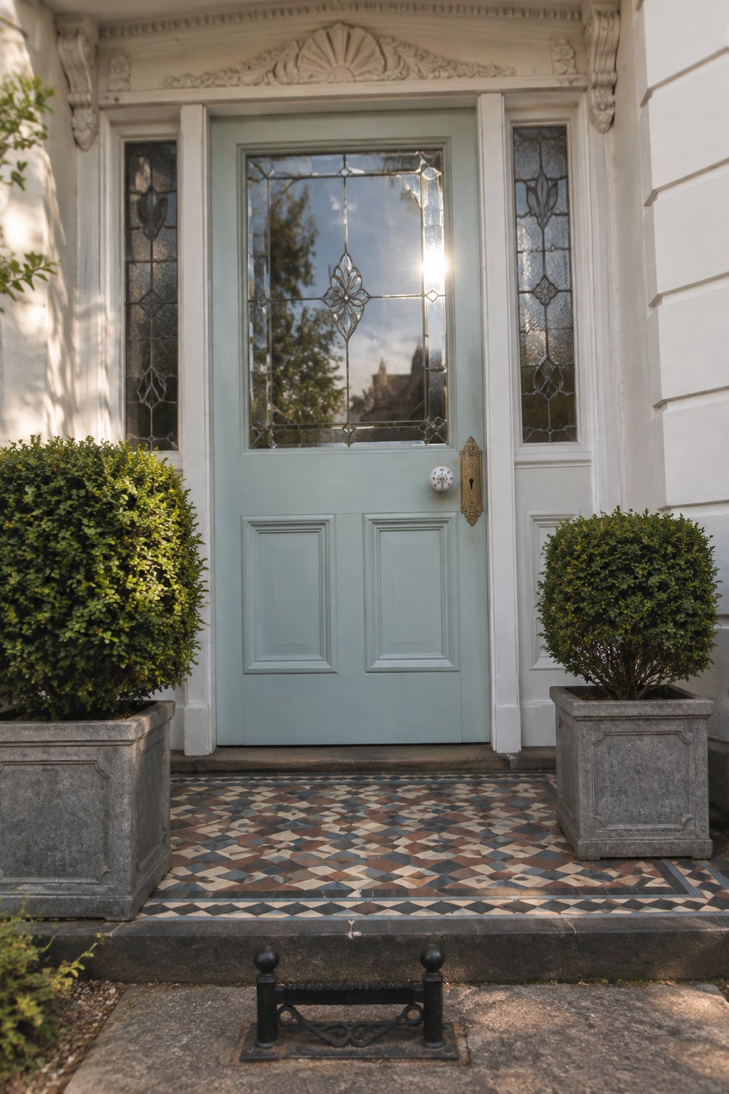 Pale blue front door with decorative glass panels, brass hardware, white trim, and patterned entry tiles.