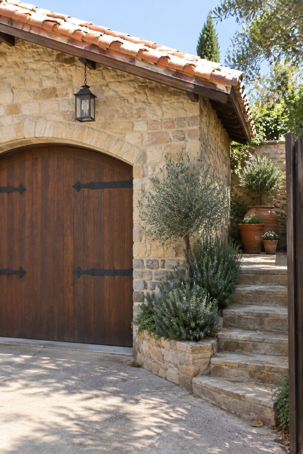 A stone stairway beside a stone house leads past an arched wooden door, with potted plants near the top.