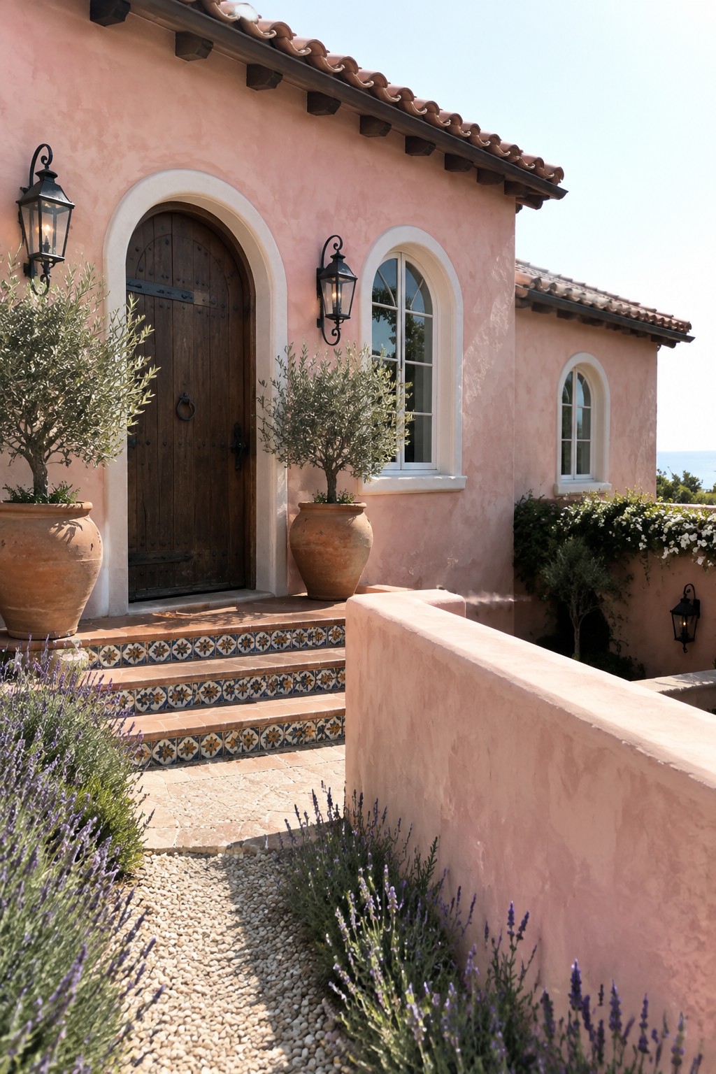 A pale pink stucco house with cream-trimmed arched windows and doorway, terracotta roof tiles, and a tiled front step.