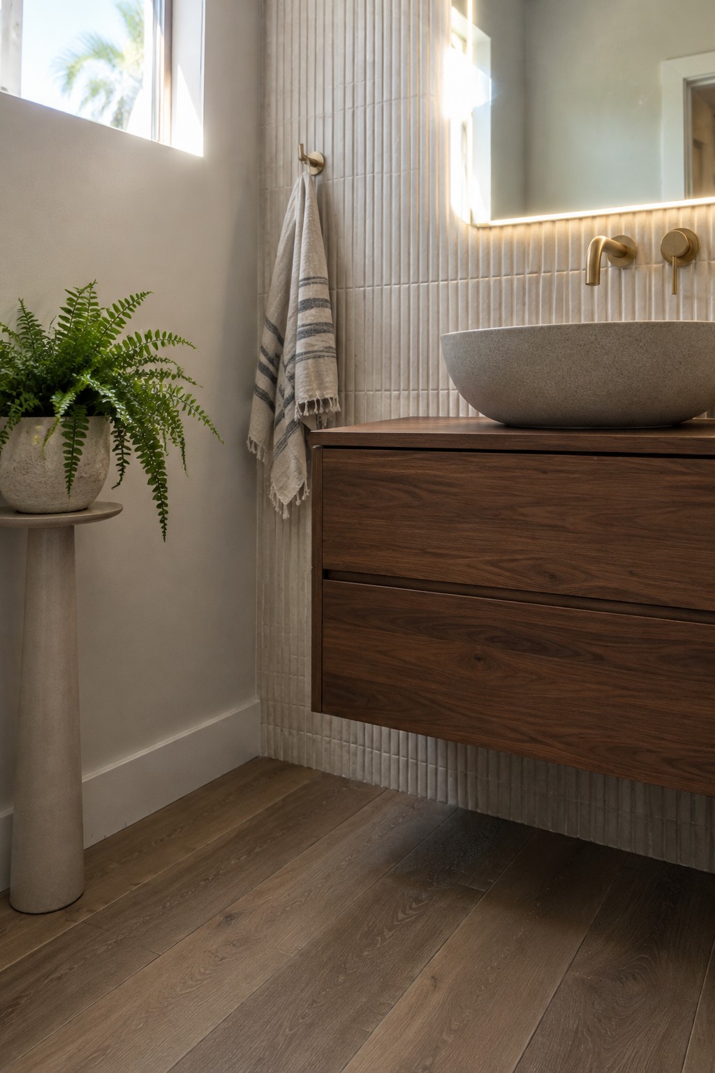 A bathroom with wide wood plank flooring, a dark wood vanity, a stone vessel sink, and vertical cream tiles.