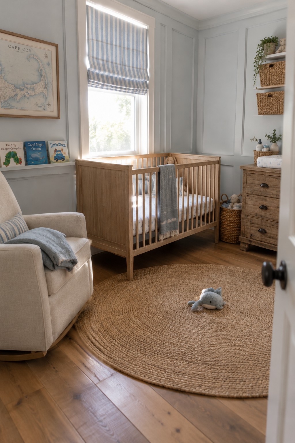 A wooden crib sits beside a window in a nursery with blue striped curtains, a cream chair, and a round woven rug.