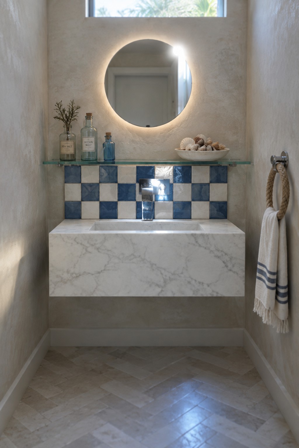 A floating marble vanity sits below a blue and cream checkerboard tile backsplash, with a round illuminated mirror above it.